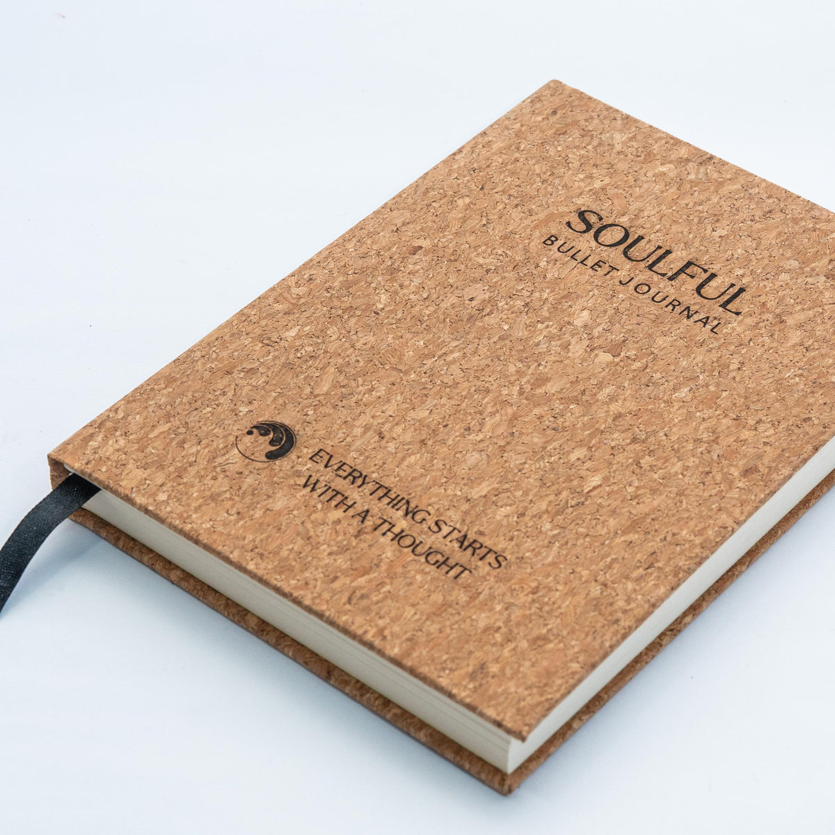 A cork-covered bullet journal with a black ribbon bookmark, shown at an angle on a clean white background. The cover features the text 'SOULFUL BULLET JOURNAL' and 'EVERYTHING STARTS WITH A THOUGHT'.