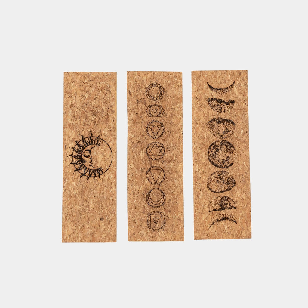 Three cork bookmarks with laser-engraved sun moon design, chakras design, and moon phase designs, on a white background