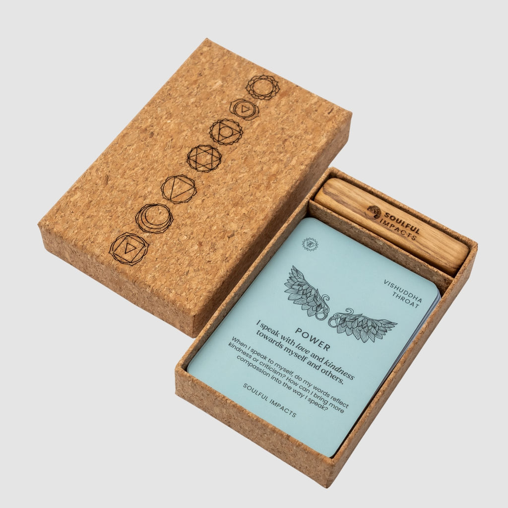 Chakra Affirmation Card Deck containing chakra-colored motivational messages, in a brown cork box, with wood card stand holder, on a white background