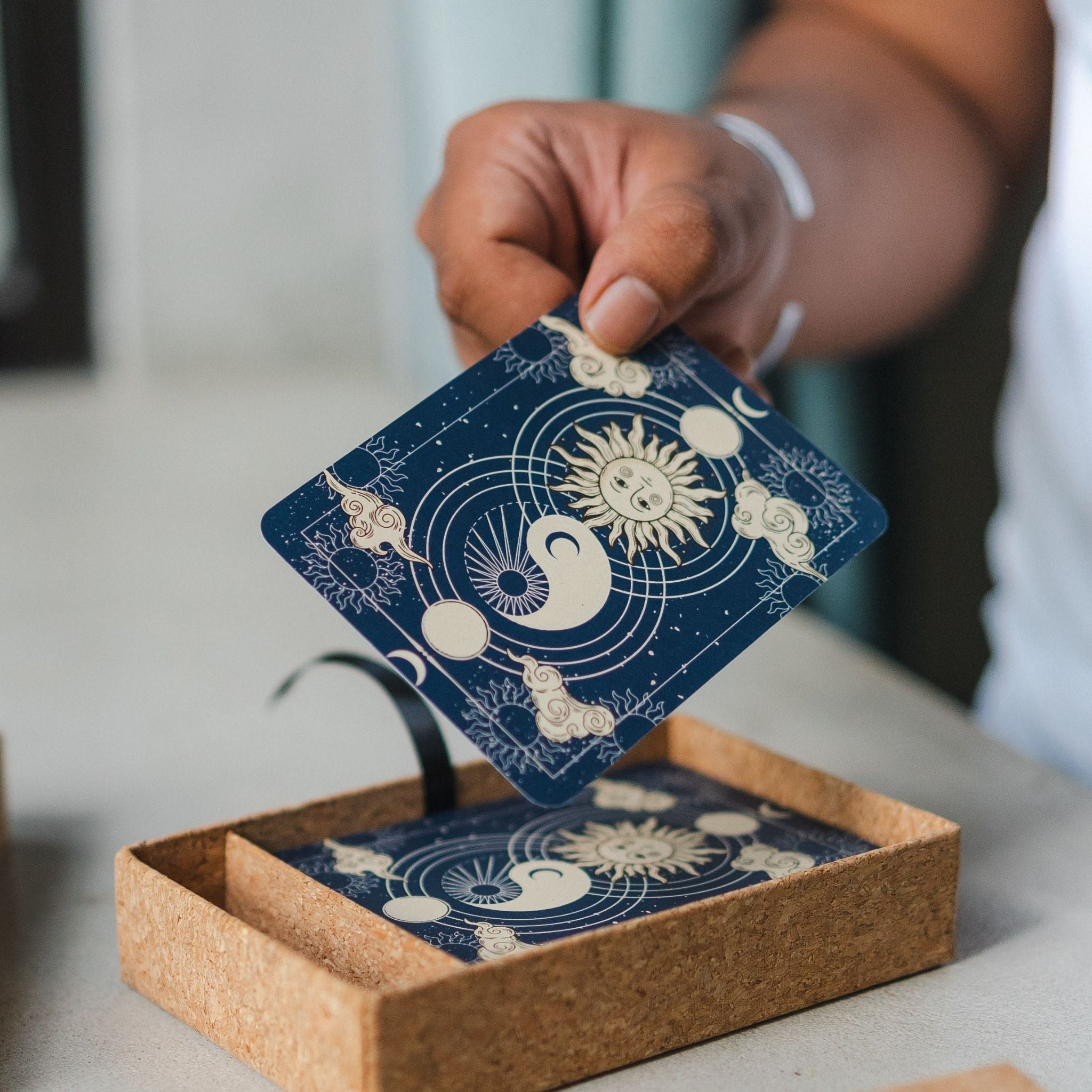 Hand holding a blue card with celestial moon card designs above an open box containing similar cards.