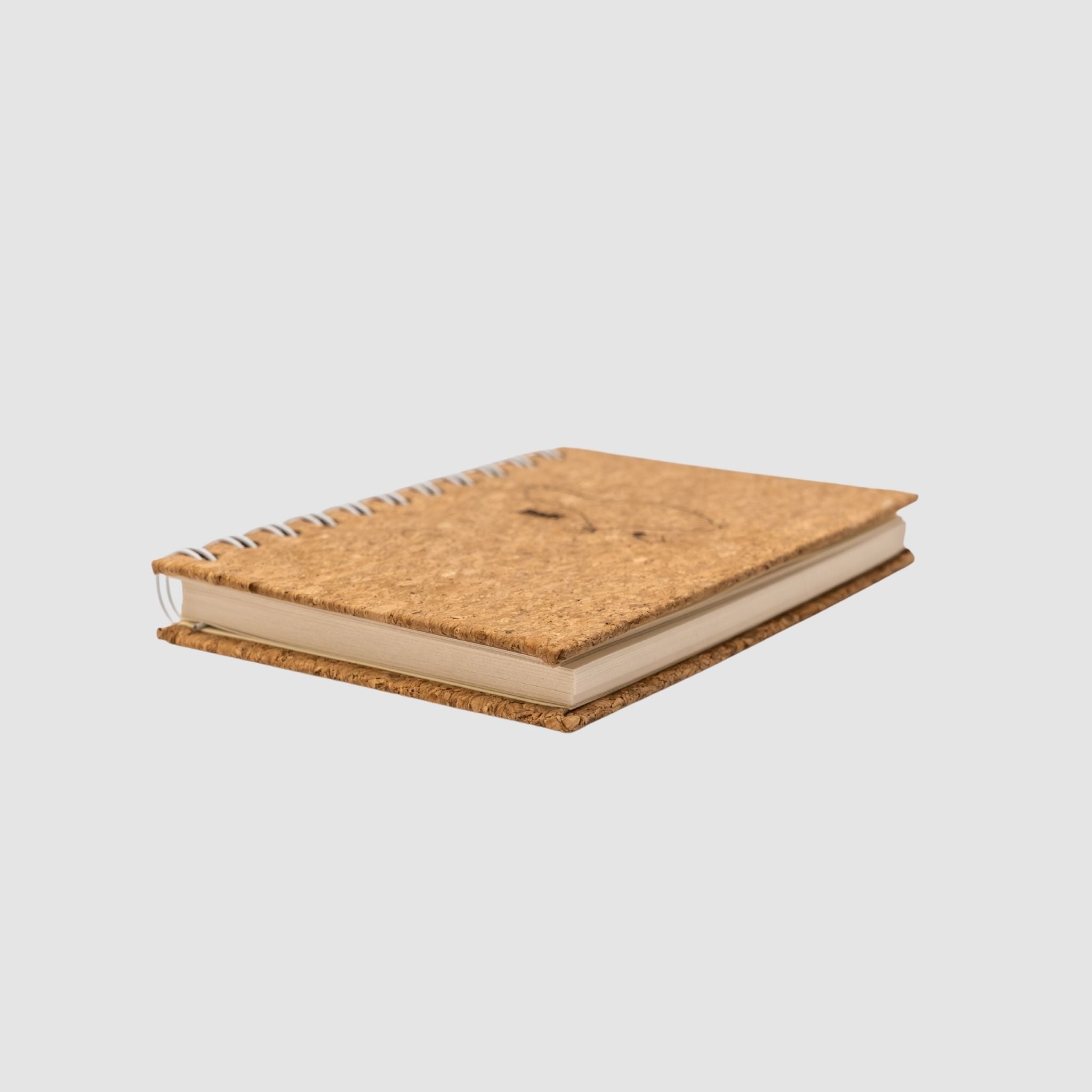 Small cork-based, compact spiral notebook, sitting on its side to show thickness, on a white background
