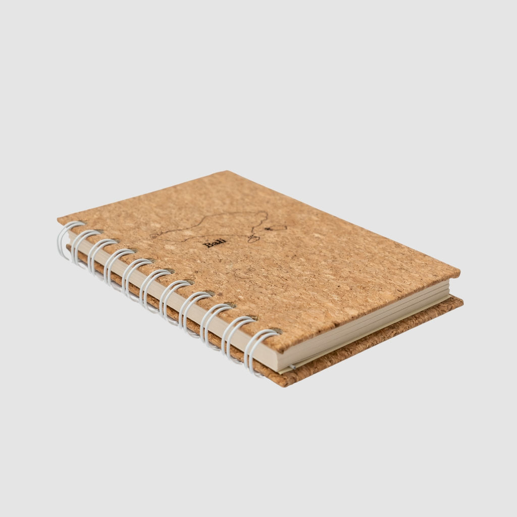 Small cork-based, compact spiral notebook, sitting on its side to show thickness, on a white background